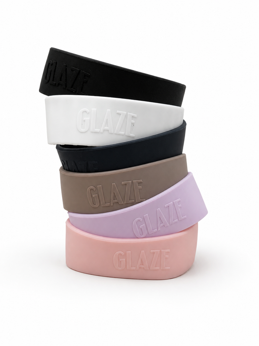 Five silicone coffee cup bands in black, white, dark navy, taupe, lavender, and light pink, stacked vertically on a white background. Each band features the brand name 'GLAZE' embossed on the front.