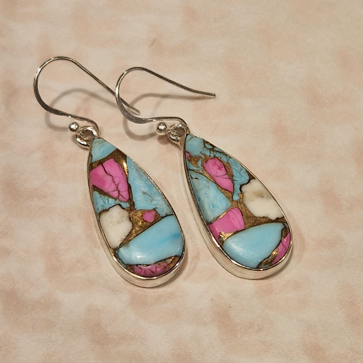Teardrop-shaped earrings with colorful stone inlay on a beige background