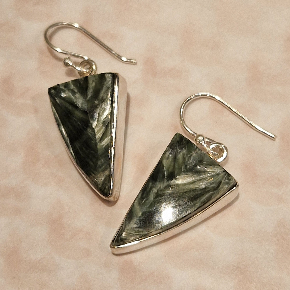 Pair of triangular earrings with green stone inlays on a beige background