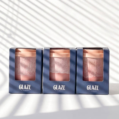 Three GLAZE reusable travel mugs in dark blue packaging, arranged side by side on a white surface with diagonal windowpane shadows.