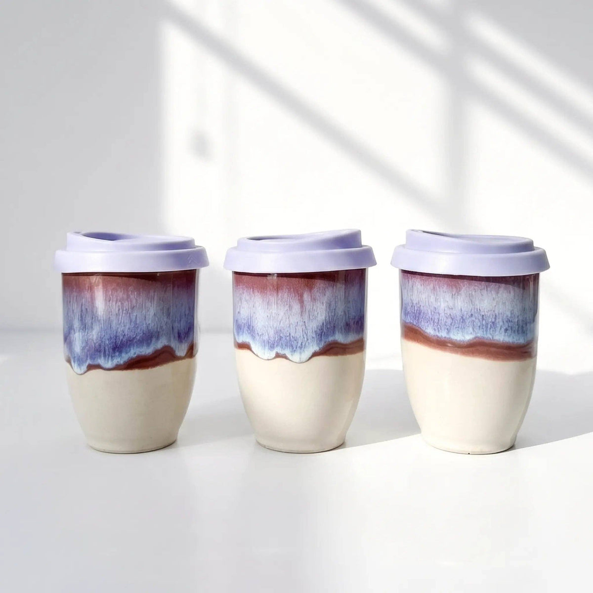 Three ceramic tumblers with purple and blue glaze on a white background