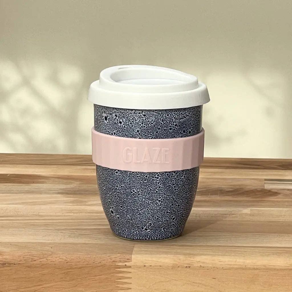 Reusable coffee cup with a pink band and white lid on a wooden surface