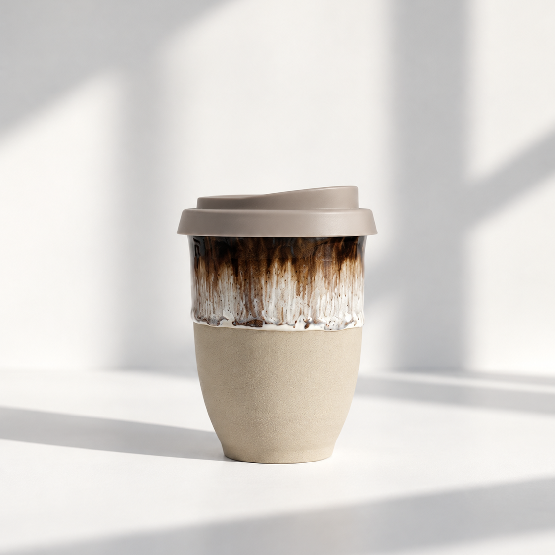 A reusable travel tumbler with a matte taupe lid, a textured beige lower half, and a glossy brown-to-white marbled upper section, set against a bright white background with soft window shadows.