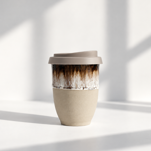 A reusable travel tumbler with a matte taupe lid, a textured beige lower half, and a glossy brown-to-white marbled upper section, set against a bright white background with soft window shadows.