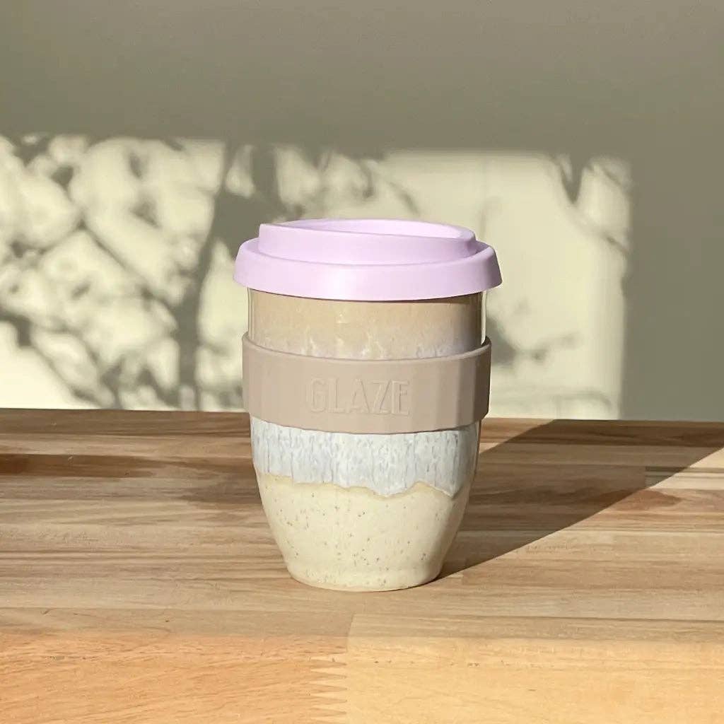 Reusable coffee cup with a pink lid on a wooden surface