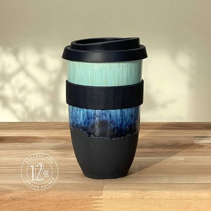 Reusable coffee cup with black lid and gradient design on a wooden surface
