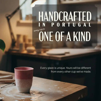 A handmade ceramic cup with a pink and white gradient glaze sits on a wooden table in a softly blurred pottery studio. Large text overlays read 'HANDCRAFTED IN PORTUGAL' and 'ONE OF A KIND', with smaller text below stating 'Every glaze is unique.