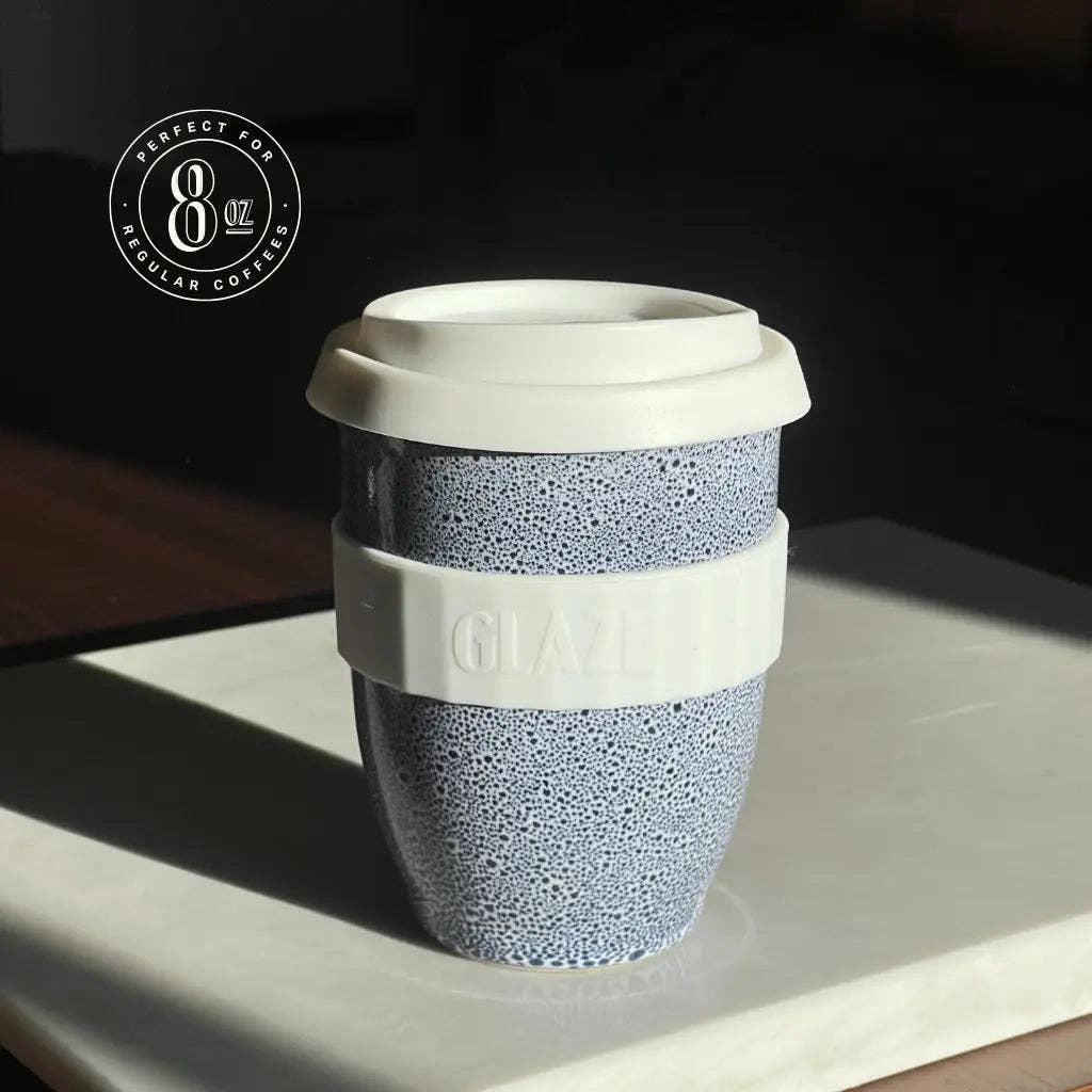 Reusable coffee cup with textured design and white lid on a reflective surface.