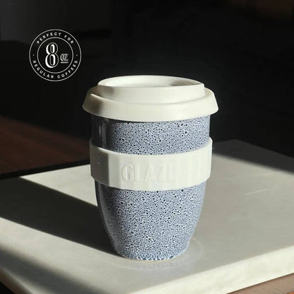 Reusable coffee cup with textured design and white lid on a reflective surface.