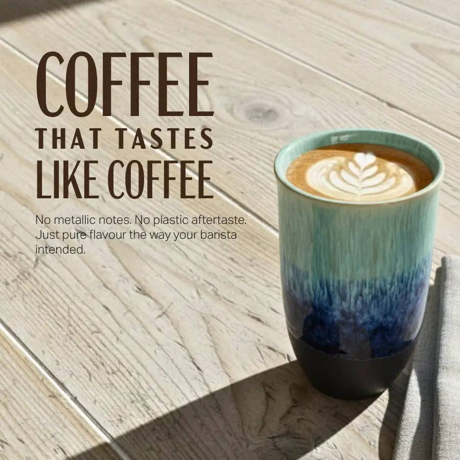 A ceramic coffee mug with a teal-to-blue gradient and a dark base, filled with latte coffee and set on a light wood tabletop. Large text on the left reads 'COFFEE THAT TASTES LIKE COFFEE' with smaller descriptive copy below.