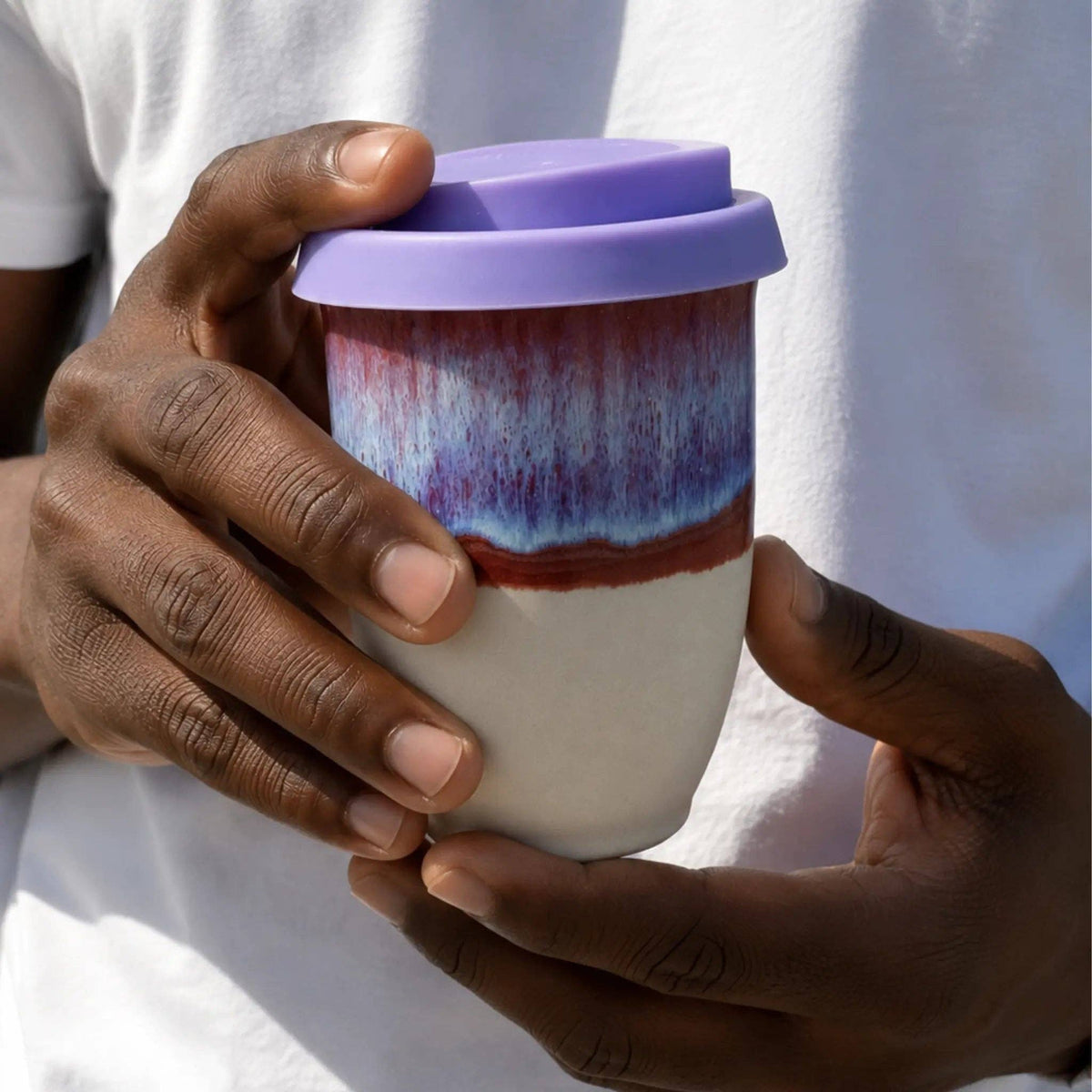 Person holding a ceramic cup with a purple lid against a white background