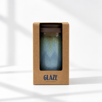 A glazed travel tumbler with a blue and teal gradient design, presented inside its brown kraft paper packaging box with a window and the brand name 'GLAZE' printed on the front.