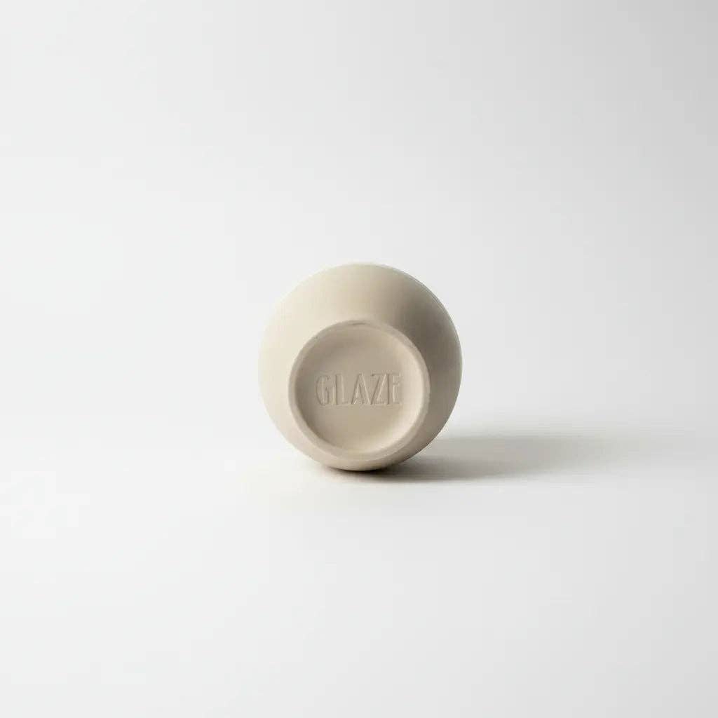 A small round ceramic cup or bowl shown from the bottom, featuring a matte beige finish and the brand name 'GLAZE' embossed in the center, set against a clean white background.