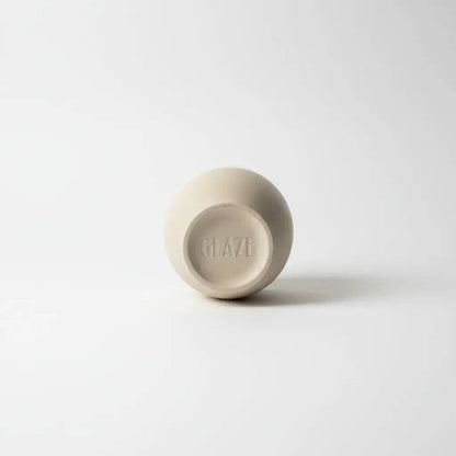 A small round ceramic cup or bowl shown from the bottom, featuring a matte beige finish and the brand name 'GLAZE' embossed in the center, set against a clean white background.