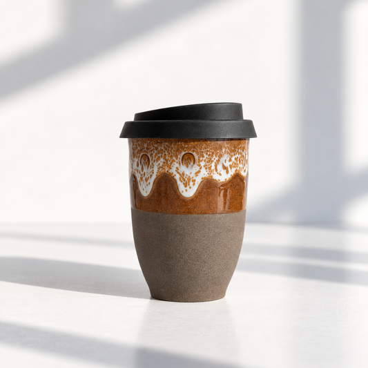 A ceramic travel tumbler with a black lid, featuring a glossy brown and white wavy patterned upper section and a matte taupe-brown lower half, set against a bright white background with soft diagonal shadows.