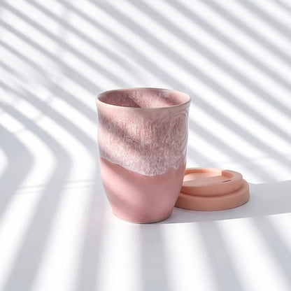 Pink ceramic cup with lid on a white surface with shadow pattern