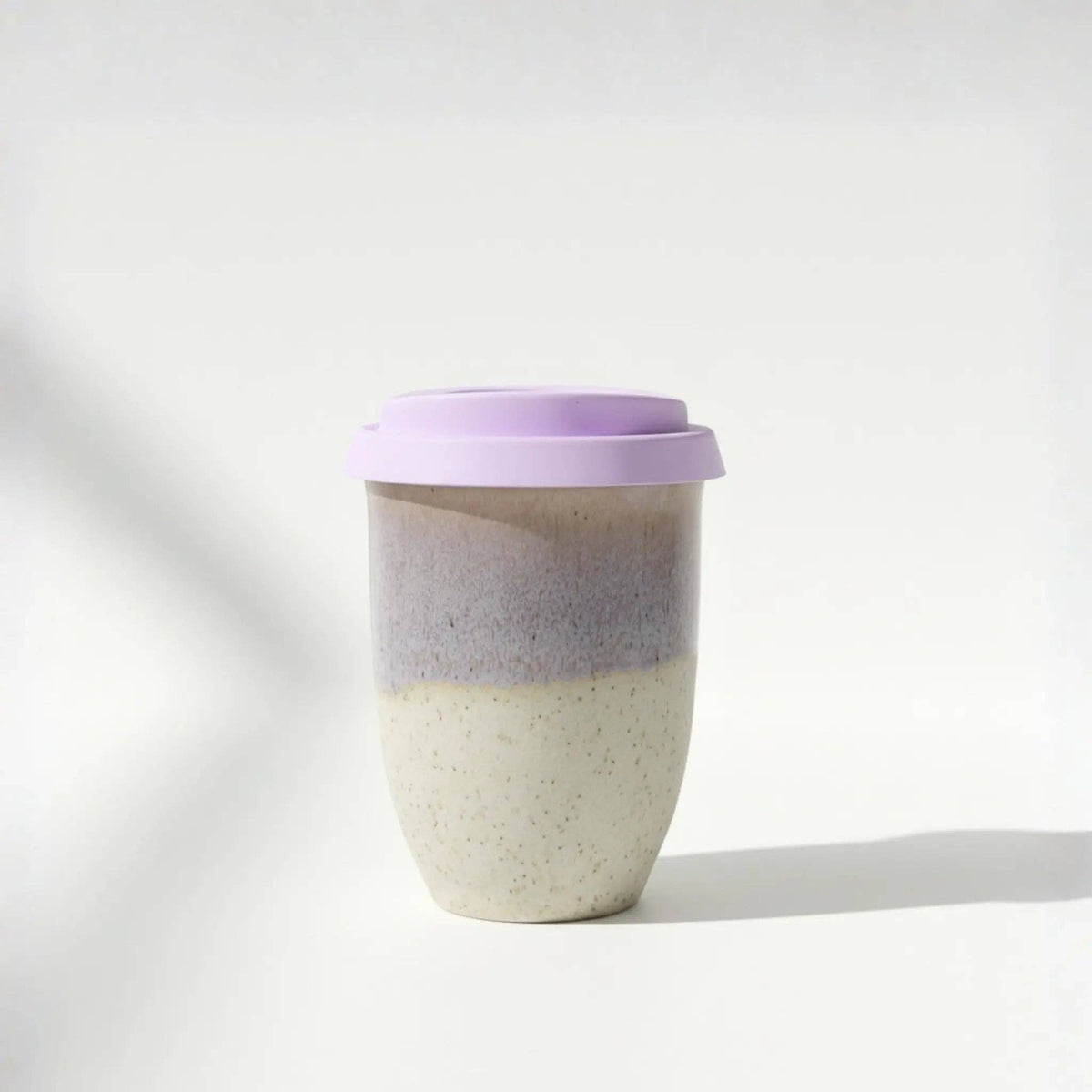 Two-toned ceramic cup with a purple lid on a white background