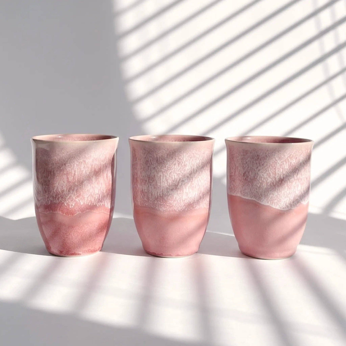 Three pink ceramic vases on a white surface with shadows from a window.