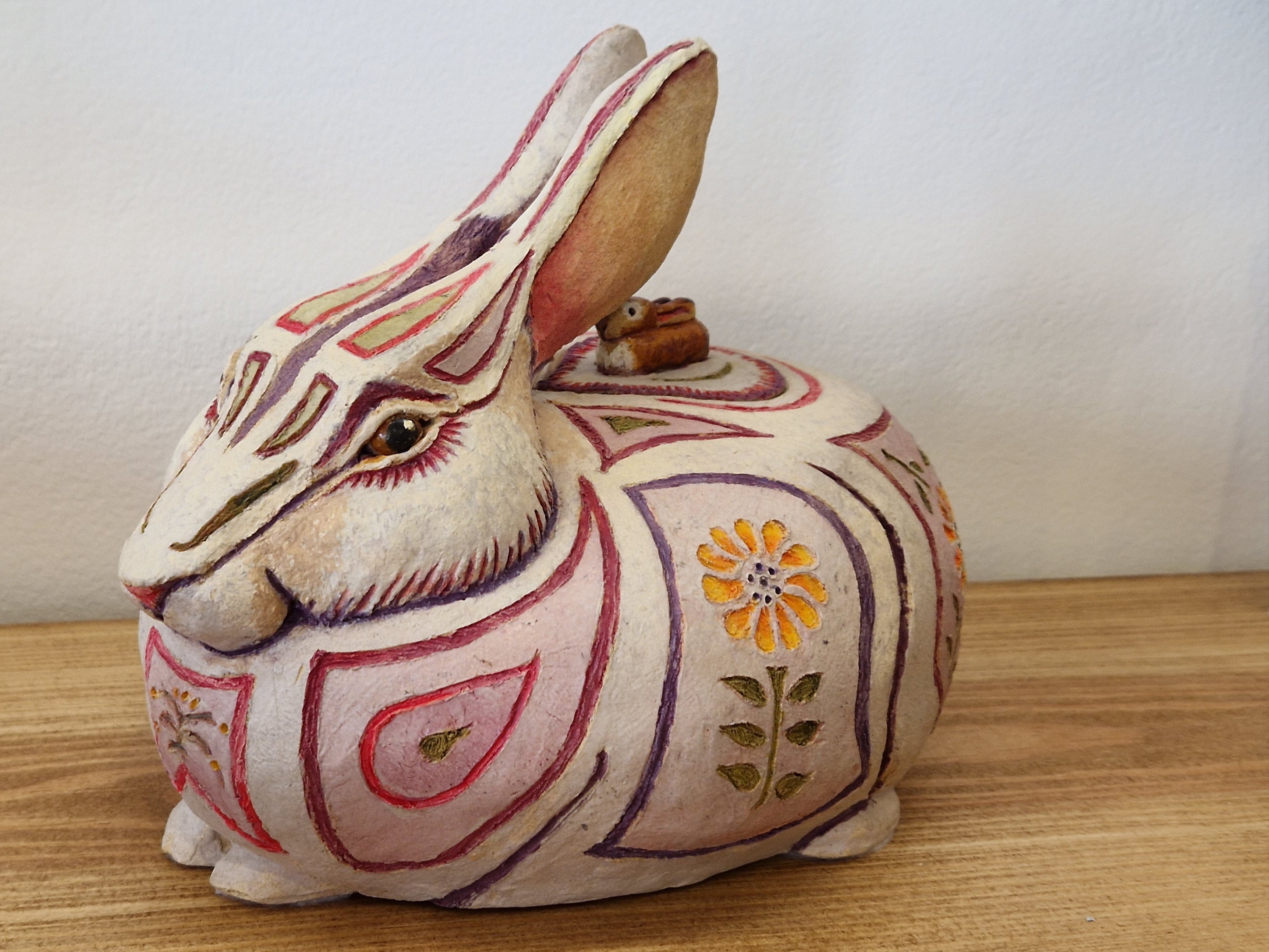 Decorative rabbit-shaped container with floral patterns on a wooden surface By Hilary Audus