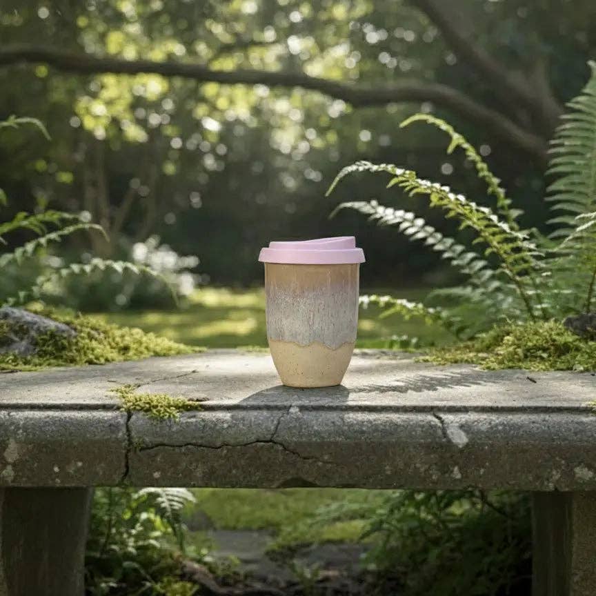 Reusable coffee cup with a pink lid on a stone surface in a garden setting
