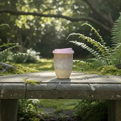 Reusable coffee cup with a pink lid on a stone surface in a garden setting