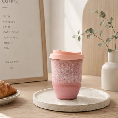 Pink ceramic cup on a white coaster with a plant and framed text in the background