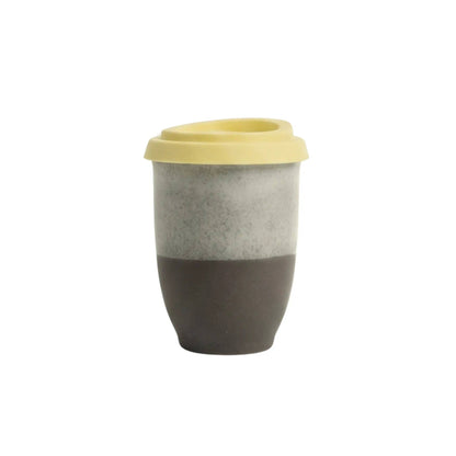 A reusable travel tumbler with a two-tone design, featuring a textured light gray upper half and a matte dark brown lower half, topped with a light yellow lid, shown on a plain white background.