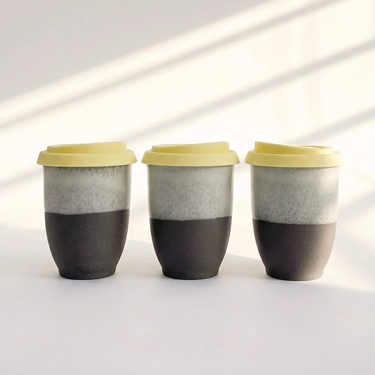 Three ceramic cups with a black bottom and gray top, featuring yellow lids on a white background.