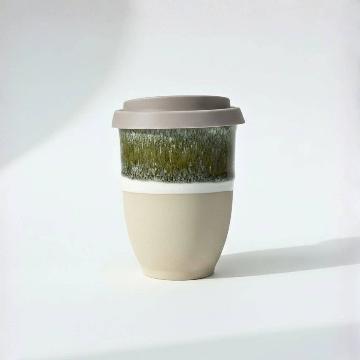 A reusable ceramic travel mug with a matte beige lower body, a textured olive-green and white glazed band, and a taupe-brown lid, shown on a clean white background.