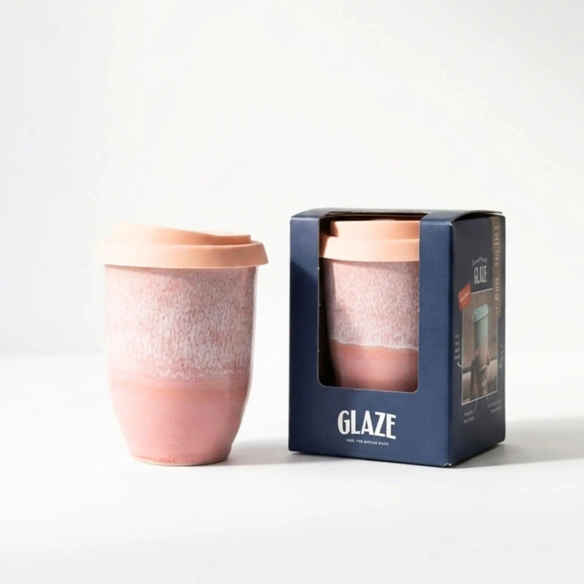 Pink ceramic cup with a matching lid next to its packaging on a white background