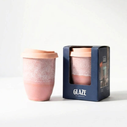 Pink ceramic cup with a matching lid next to its packaging on a white background