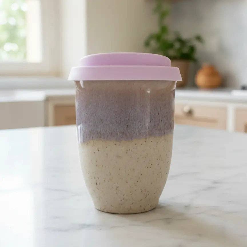 Two-toned ceramic cup with a pink lid on a marble surface in a kitchen setting.