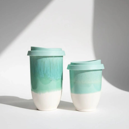 Two reusable travel tumbler cups with matching lids, featuring a white lower half and a mint green upper half with a textured vertical pattern, set against a white background with soft diagonal shadows.