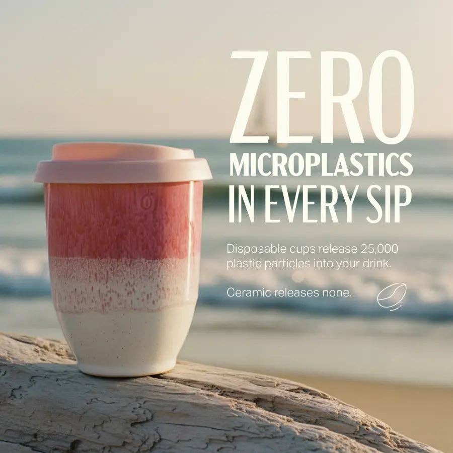 A reusable tapered travel cup with a pink-to-white gradient and a light pink lid sits on a weathered log by the ocean, with large white text on the right reading 'ZERO MICROPLASTICS IN EVERY SIP' and smaller product copy below.