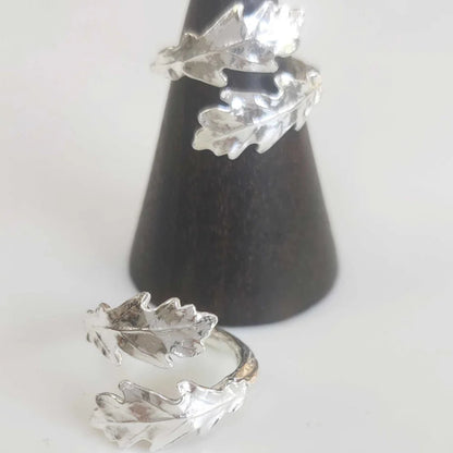Silver leaf-shaped earrings on a black cone stand against a white background