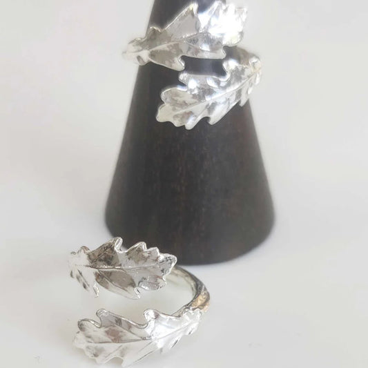 Silver leaf-shaped earrings on a black cone stand against a white background