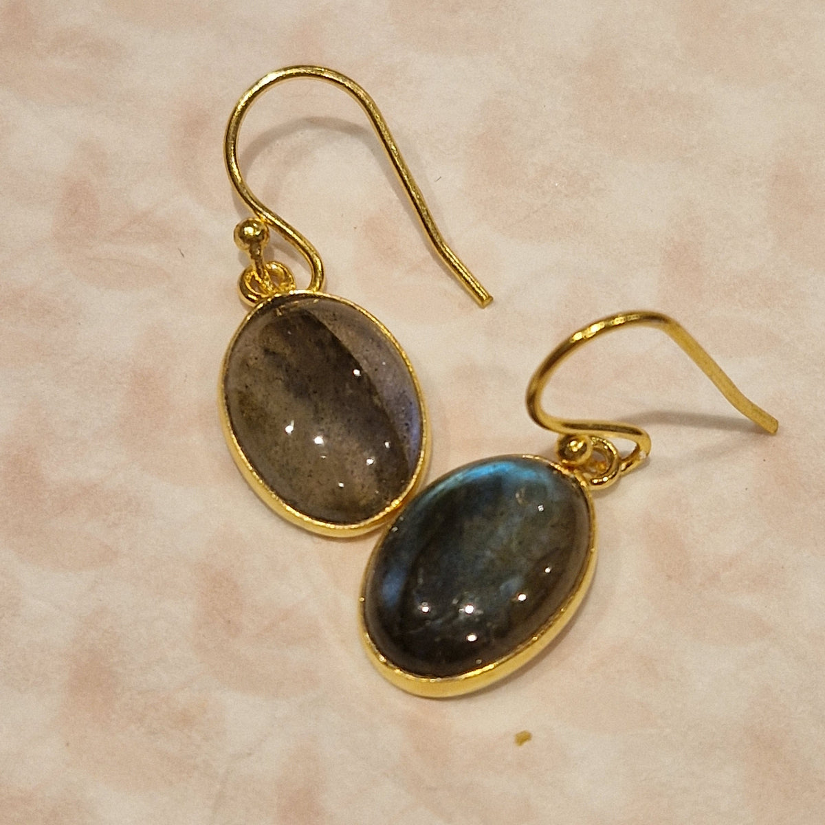 Gold earrings with oval gemstones on a beige background