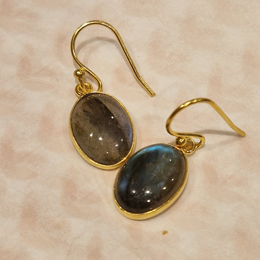 Gold earrings with oval gemstones on a beige background