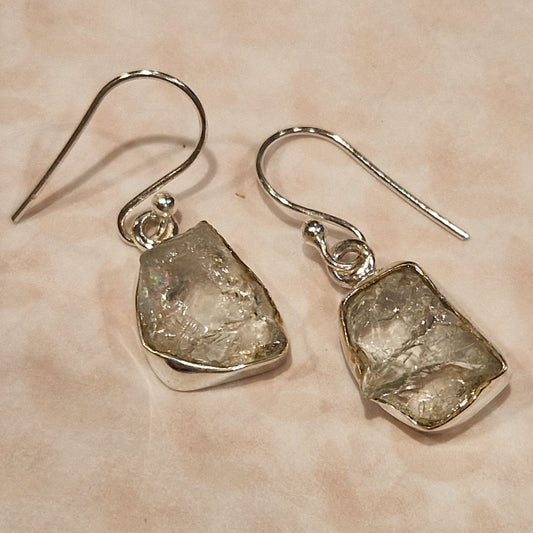 Silver earrings with rough stone-like ends on a beige background