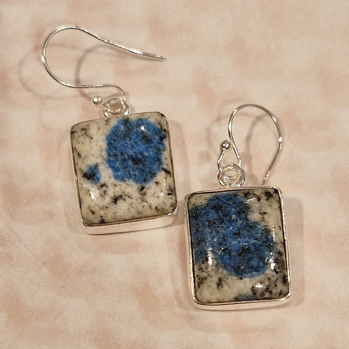 Square earrings with blue and beige pattern on a pink background