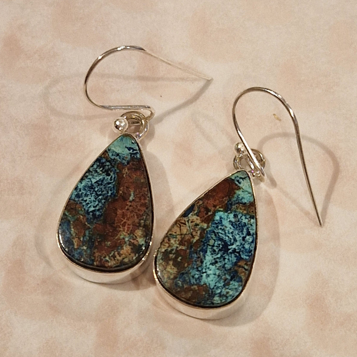 Teardrop-shaped earrings with blue and brown speckled stones on a beige background
