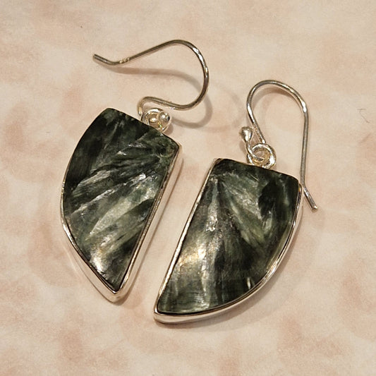 Pair of earrings with green stone and silver hooks on a beige background