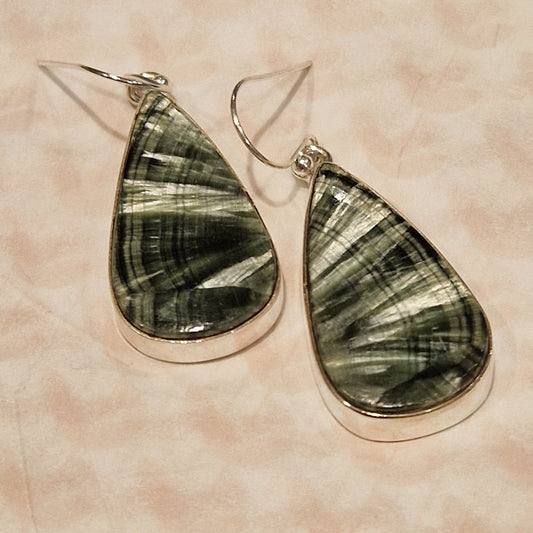 Teardrop-shaped seraphinite earrings on a beige background