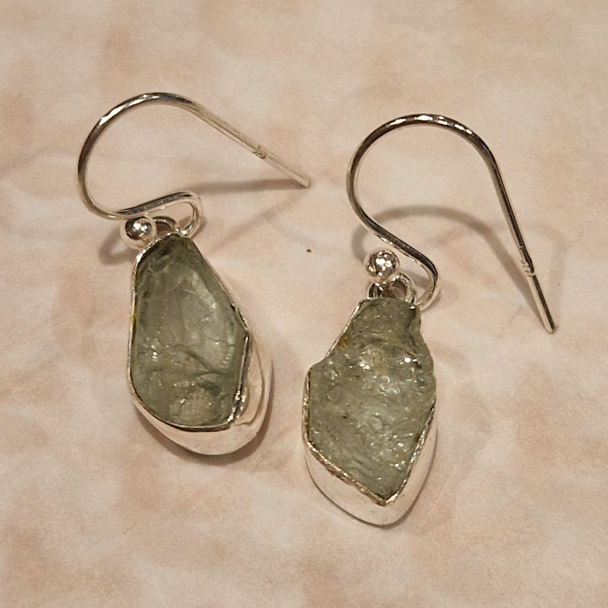 Pair of earrings with green stone drops on a beige background