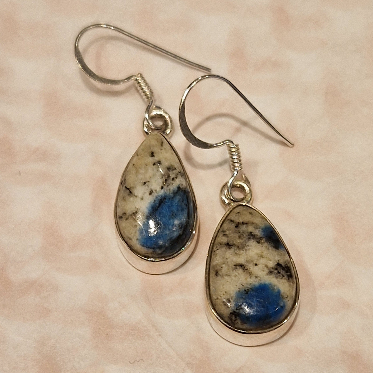 Pair of earrings with teardrop-shaped gemstones on a beige background